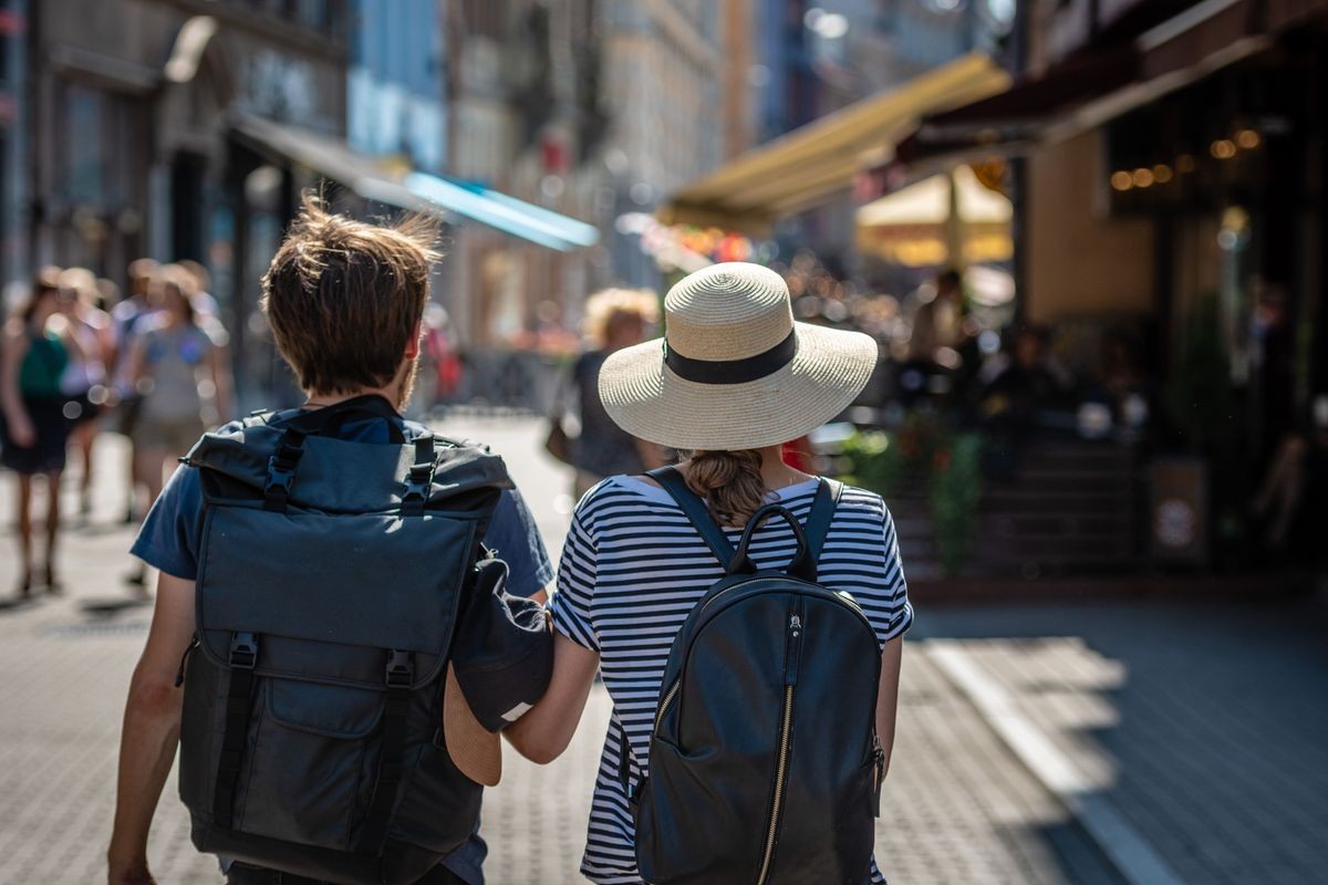 A couple of people with backpacks walking along the street. View from the back.